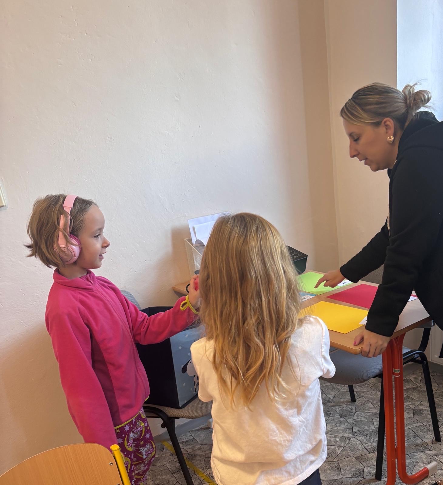 Učitelka vede cvičení s barevnými papíry u stolu